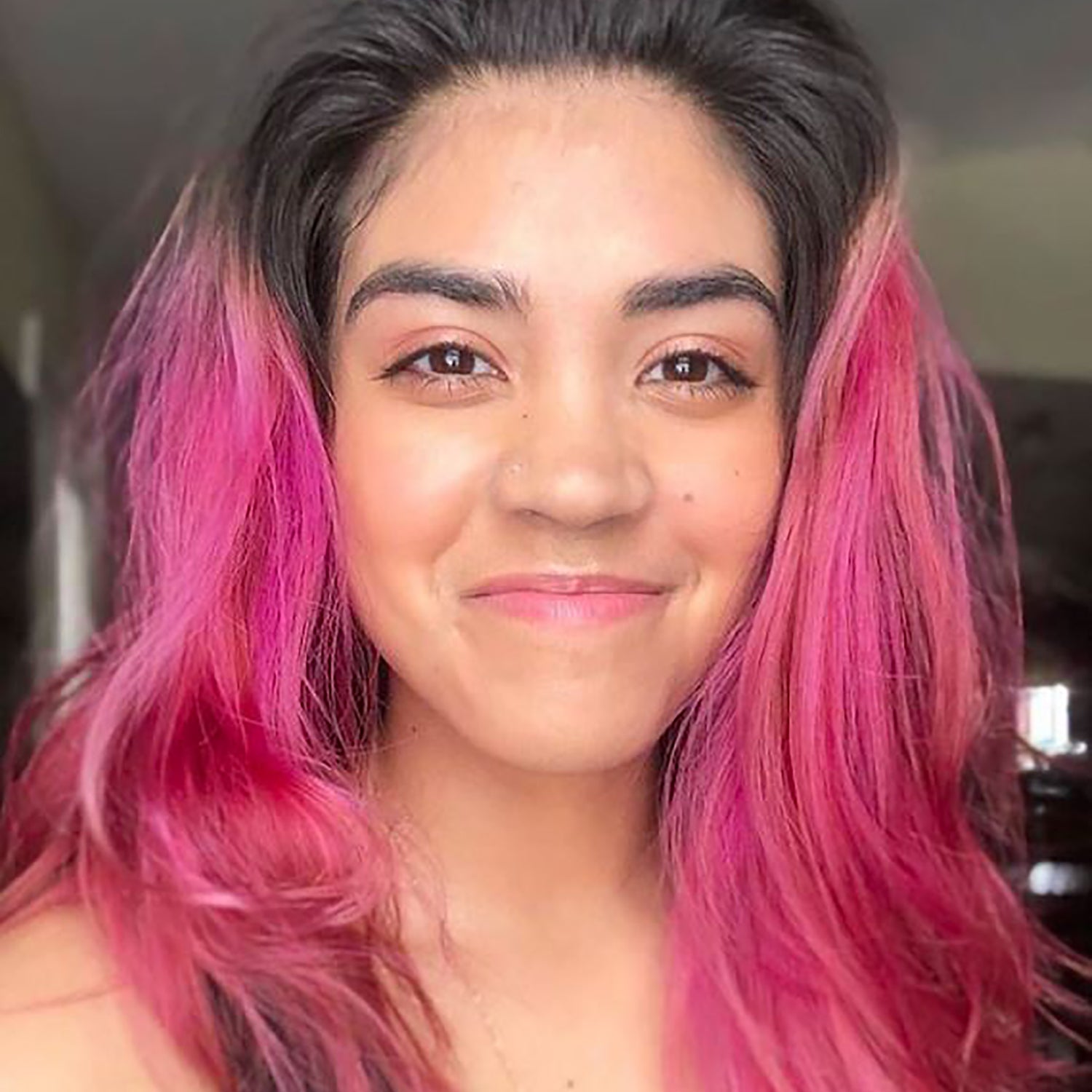 person with dark roots and vibrant magenta hair color on medium length, pre-lightened hair