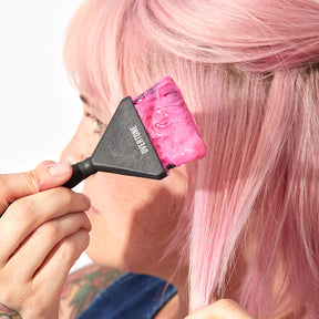 person with pastel pink hair applying pink hair color with black application brush