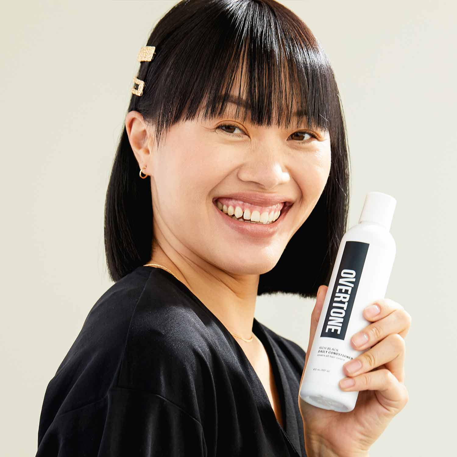 person with strait black hair color with short hair and bangs holding oVertone rich black daily conditioner
