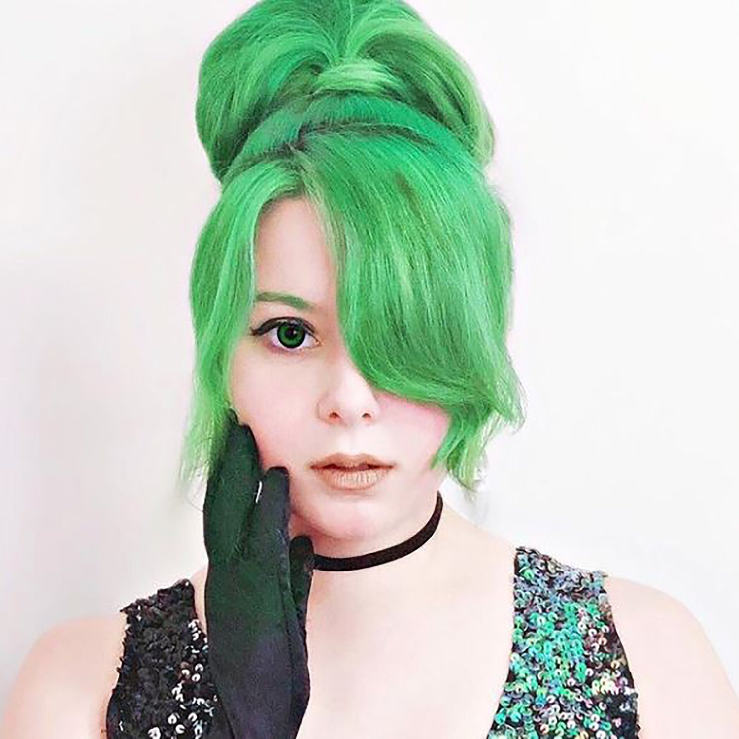 person with bright green, pre-lightened hair in a high ponytail with bangs wearing black gloves and sequin top