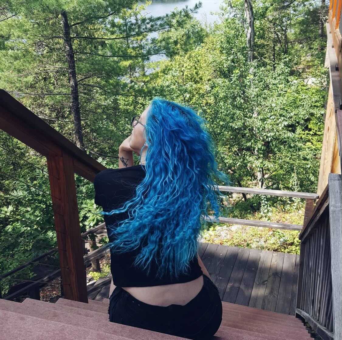 person with long turquoise hair color on pre-lightened curly hair